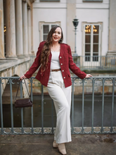 a lady wears a red tweed jackt with a white top and white pants